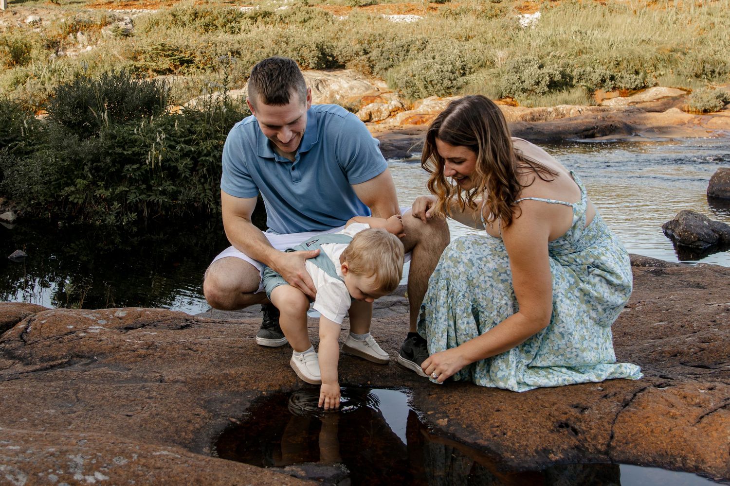 People sit on red rocks near a stream enjoying nature and spending time together outdoors.