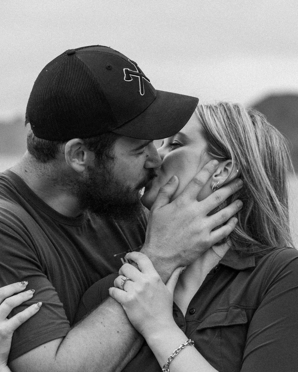 A romantic black and white photo captures an intimate kiss between two people wearing casual clothing outdoors.