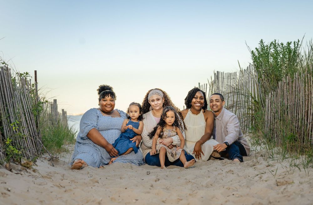 A loving family sits together on sandy dunes at the beach during sunset.