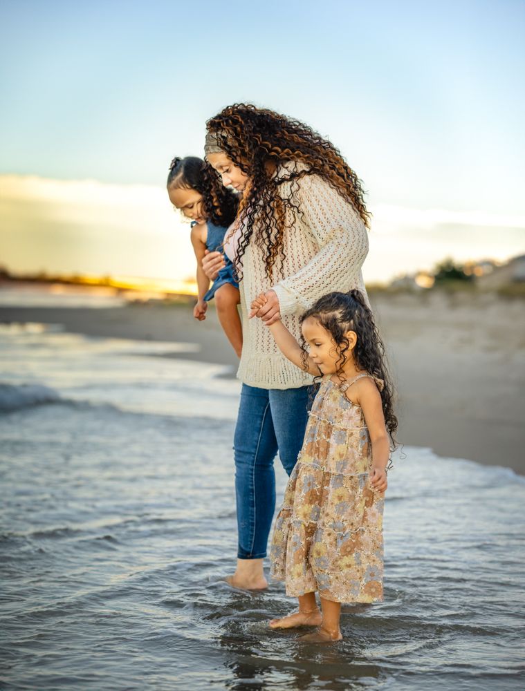 A mother and grandchildren play together at the edge of the ocean waves during sunset.