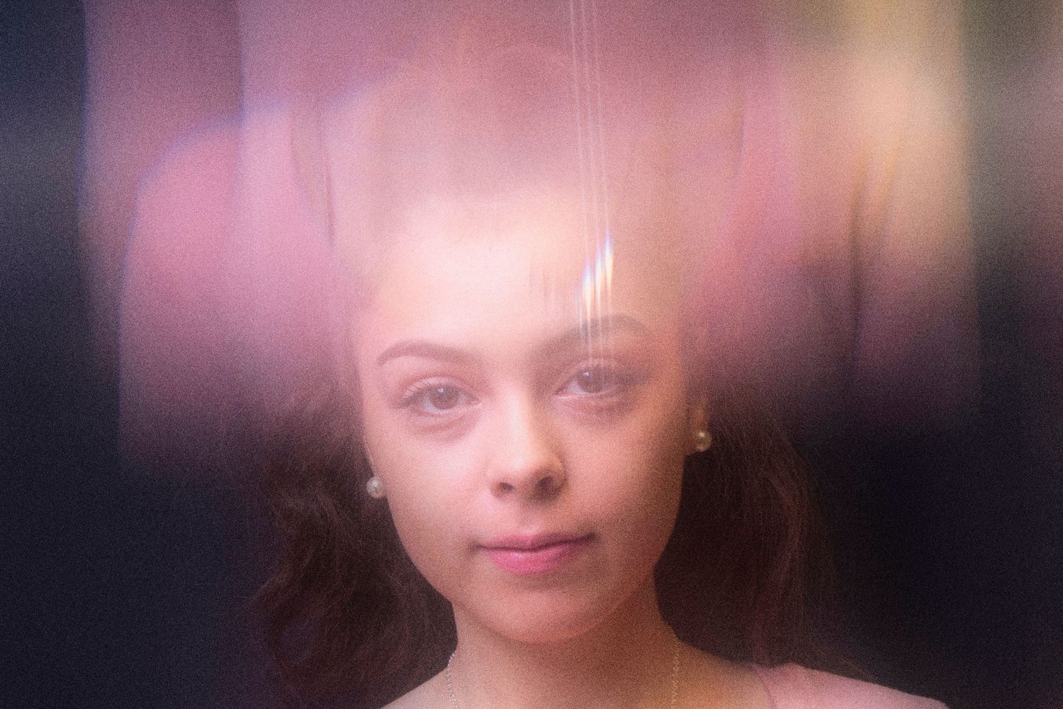 Ethereal portrait with soft pink lighting and dreamy bokeh effects.