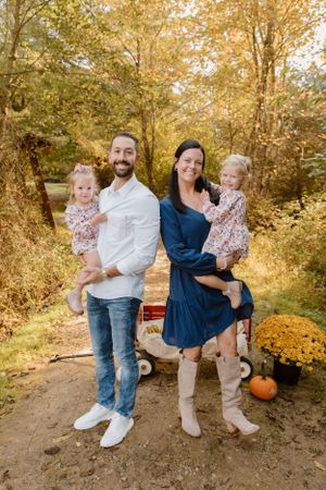 Fall family portrait with red wagon and autumn decorations on dirt path.