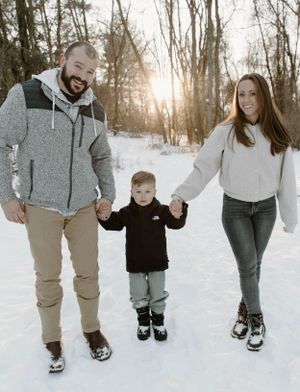 Family enjoying winter walk together on snowy trail through woods at sunset.