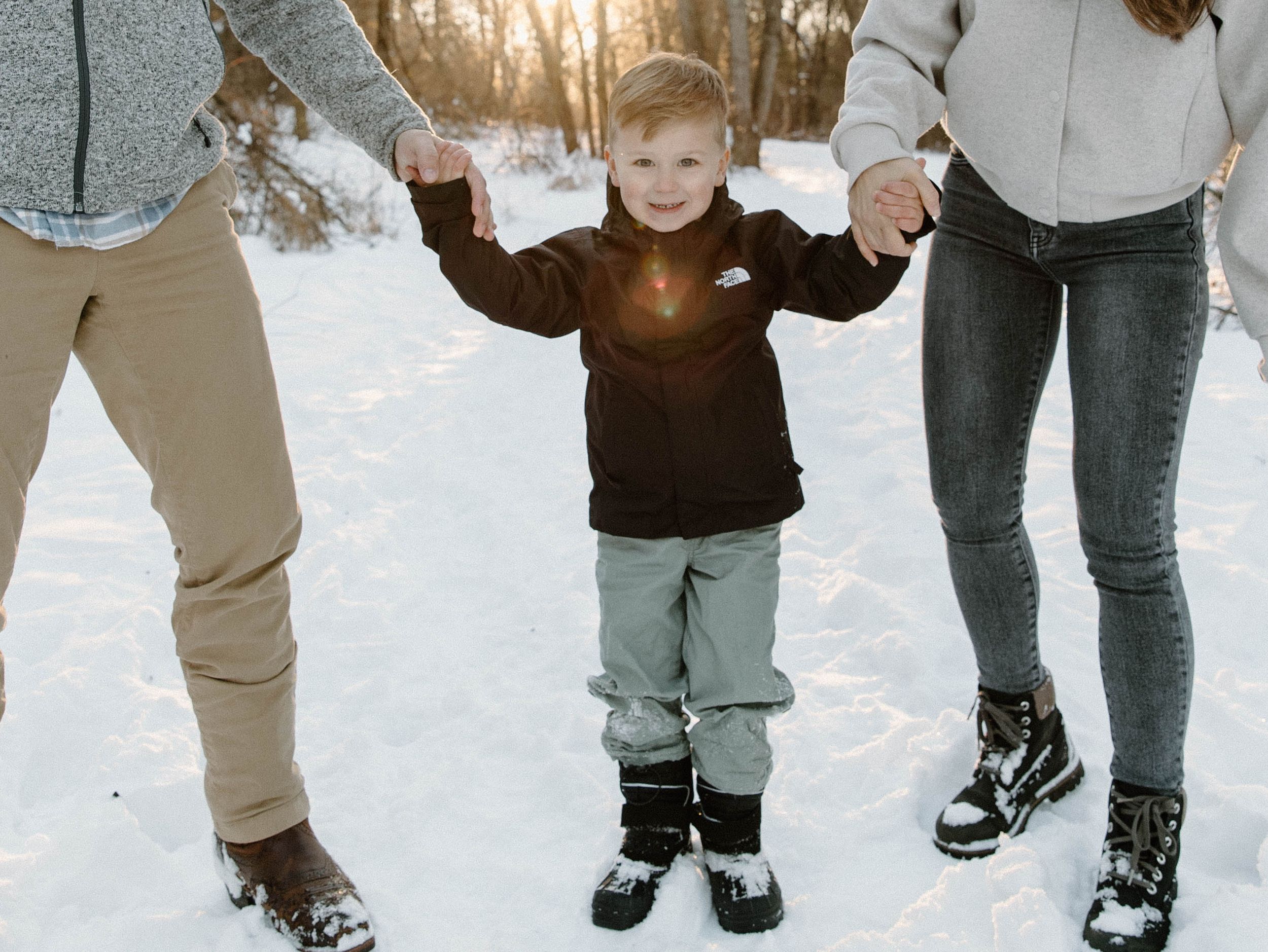 Child holding hands with parents while standing in snowy winter scene.