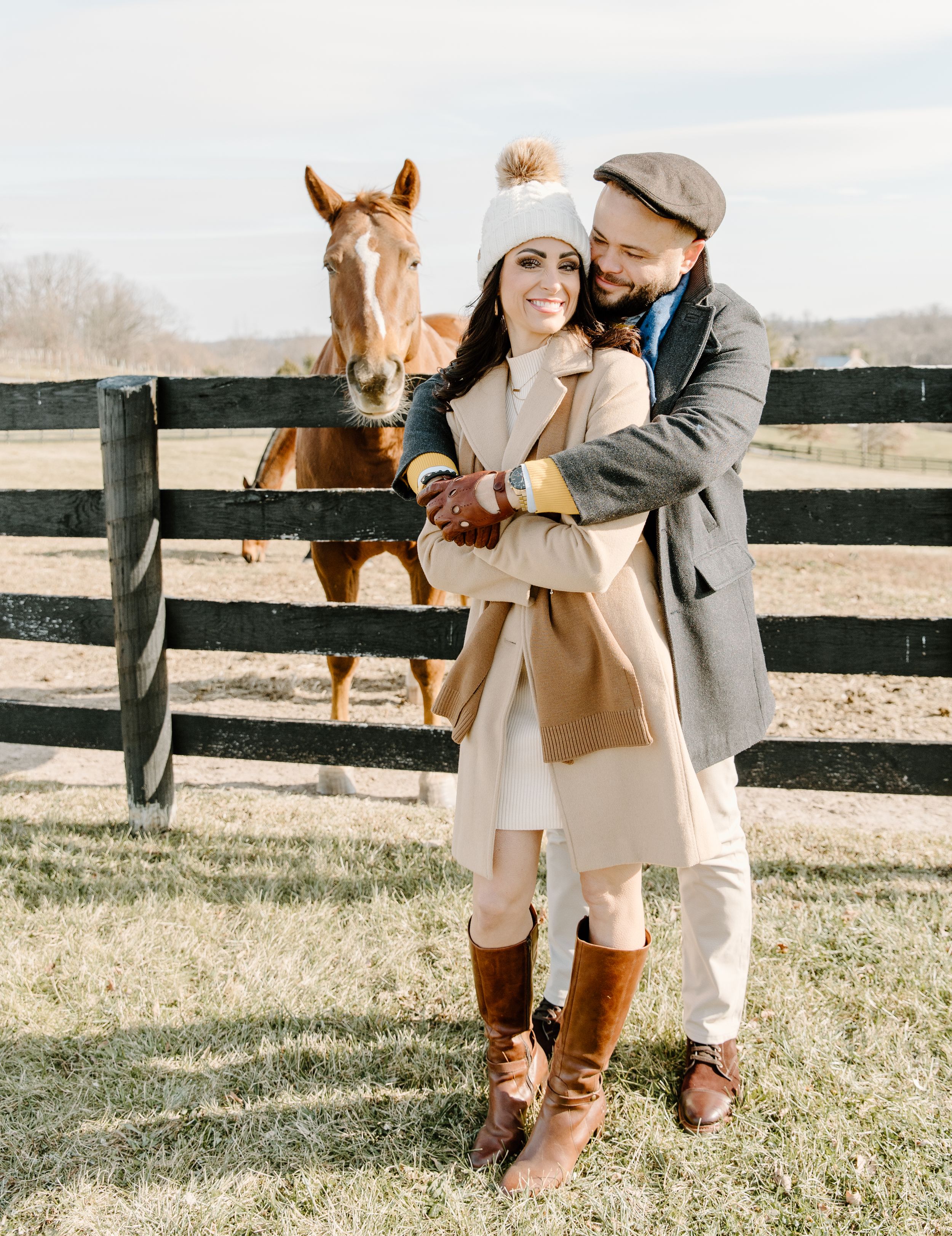 A cozy winter scene with a friendly horse peeking over a wooden fence at two visitors.