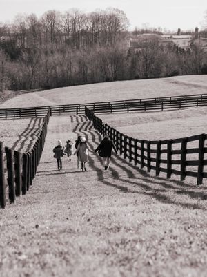 A black and white photograph of people walking along a fenced path through rolling hills.