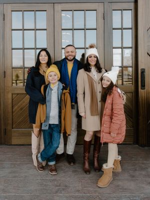 A winter family portrait in front of wooden doors wearing coordinated winter outfits.