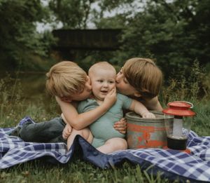 Three children sharing tender moment on picnic blanket with camping lantern.