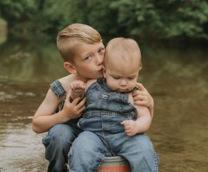 Two children in denim sitting by water's edge sharing sweet moment.