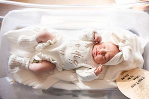 A sleeping baby in white clothing lies peacefully on a soft white blanket.