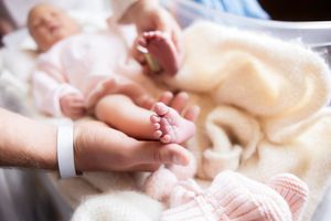Close-up of a parent holding tiny newborn baby feet in a hospital setting with a soft pink blanket.