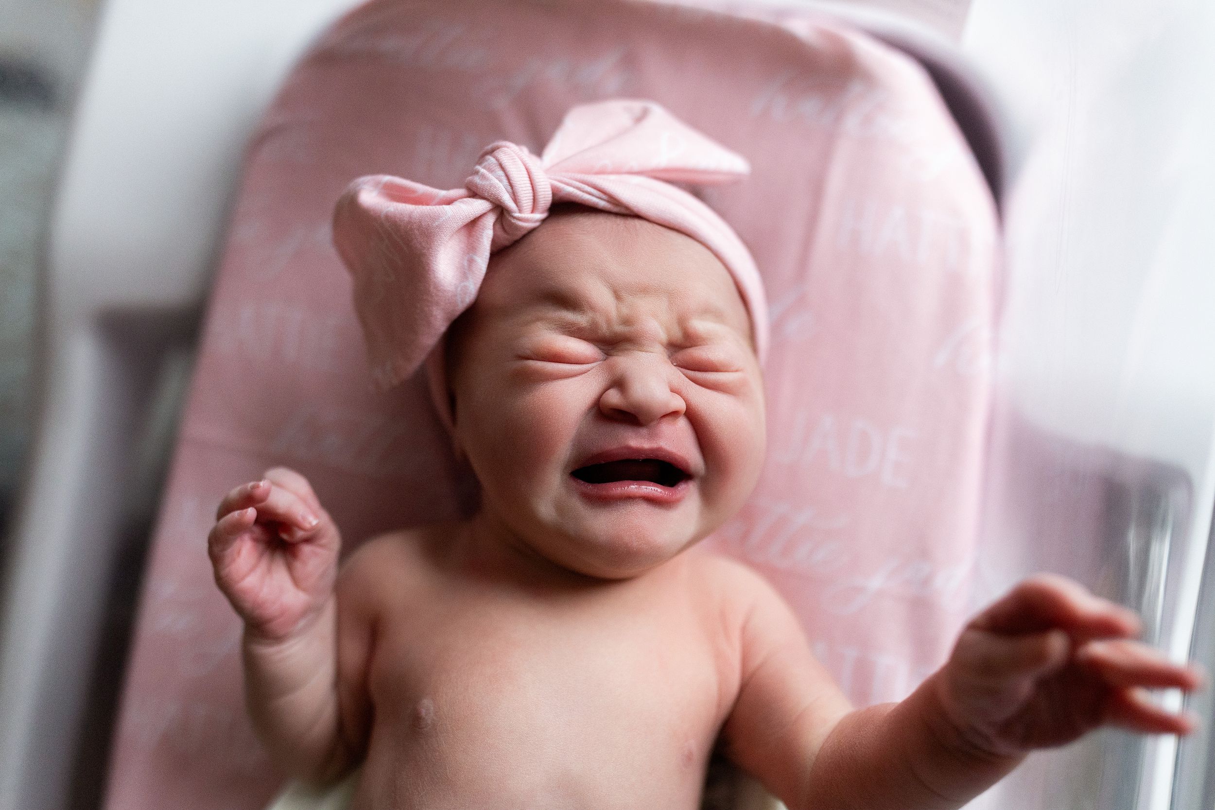 A series of candid expressions showing a baby's changing emotions from crying to laughing on pink bedding.