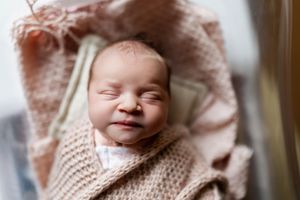 Peaceful sleeping newborn wrapped in soft knitted blanket and pink swaddle smiles contentedly.