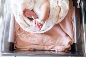 Tiny newborn feet peek out from a floral swaddle blanket on pink bedding.