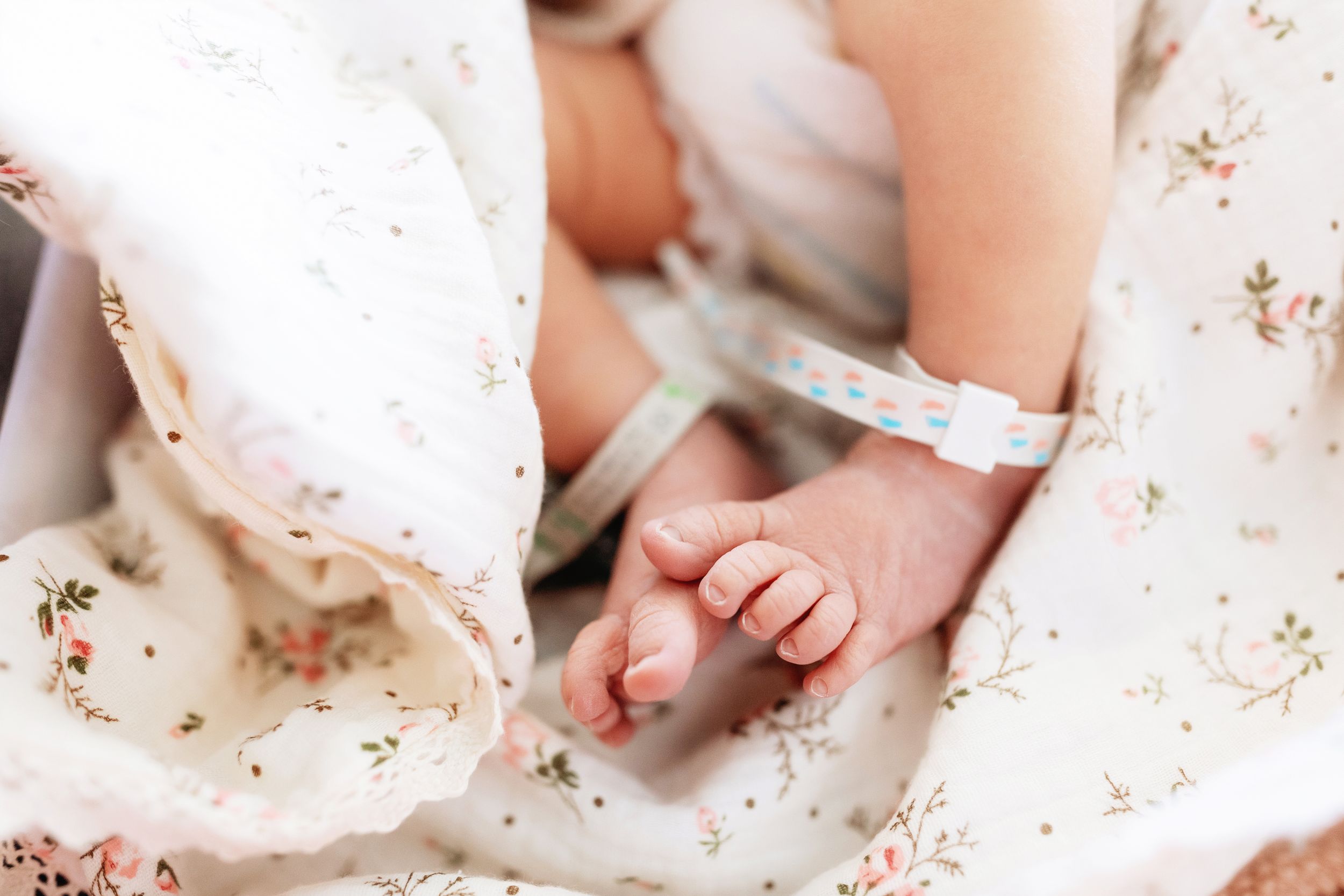 Detail shot of infant hand reaching out from floral patterned swaddle.