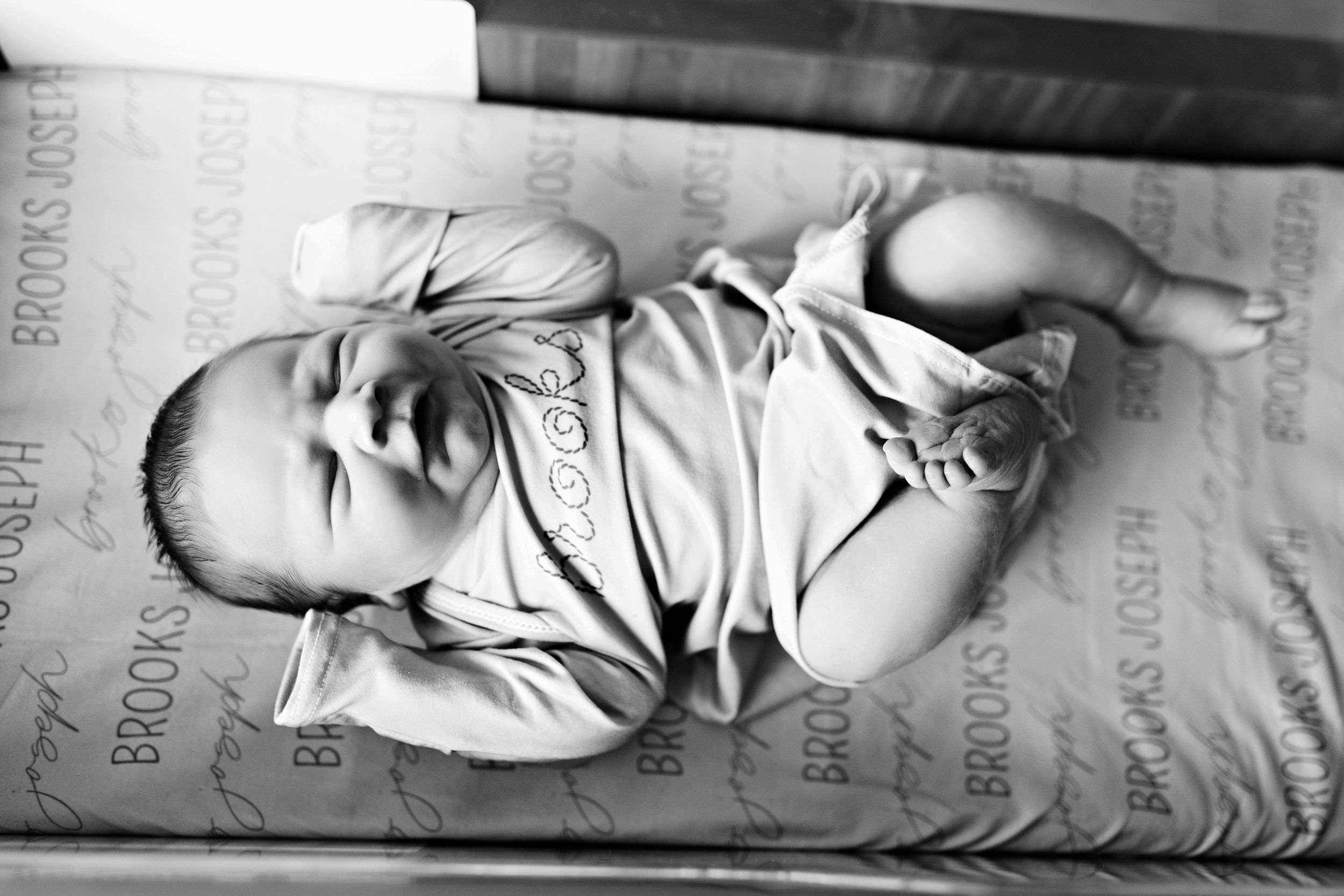 Black and white image of a newborn baby lying on their back in a hospital bed.