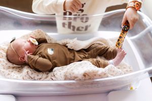 Baby resting on a textured white photography backdrop while wearing brown clothing.