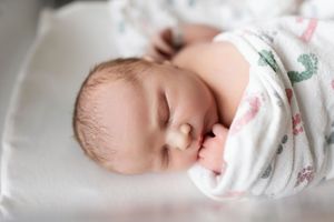Peaceful sleeping newborn baby wrapped in floral swaddle blanket rests in soft natural light.