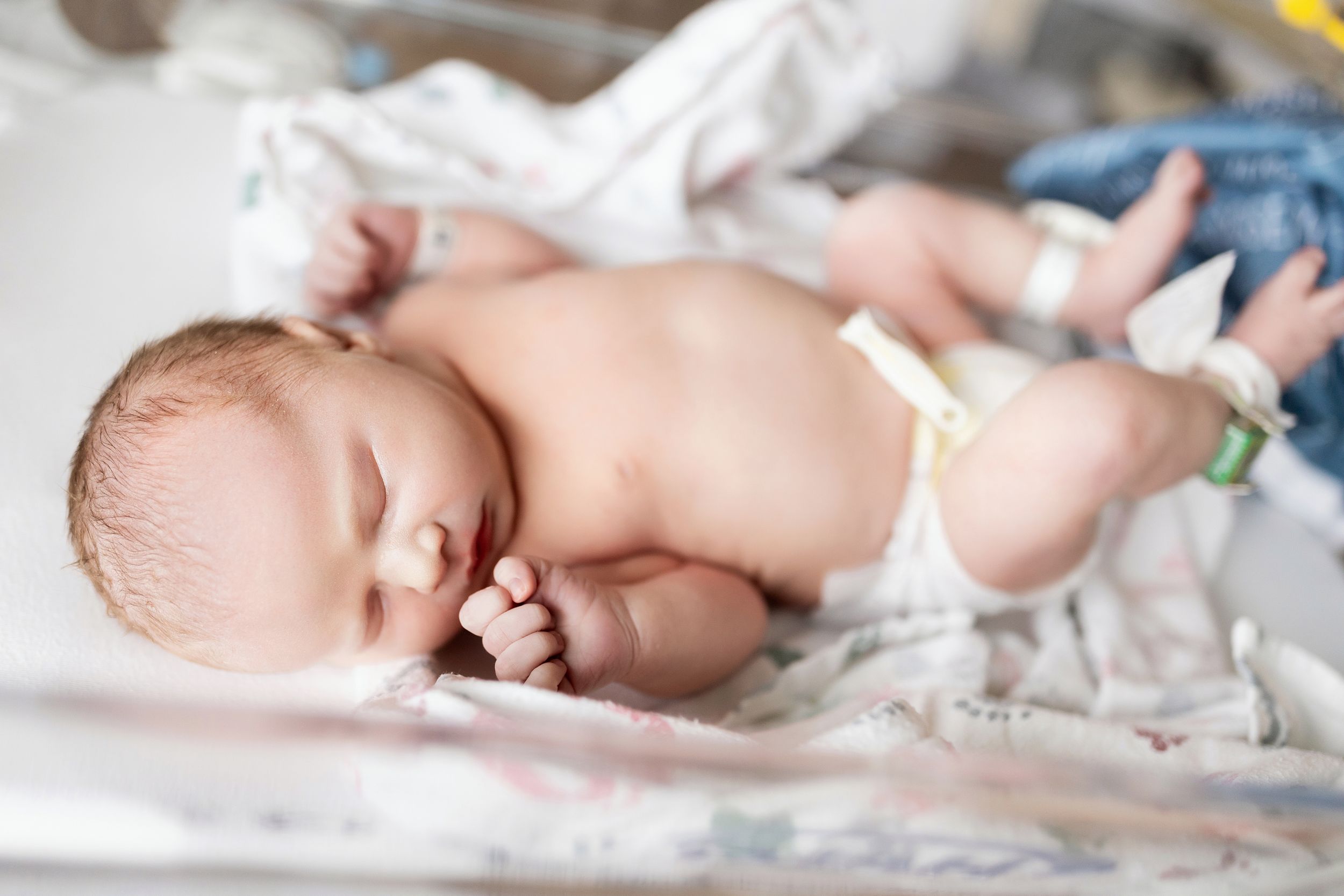 A newborn baby sleeps peacefully on white bedding while wearing only a diaper.