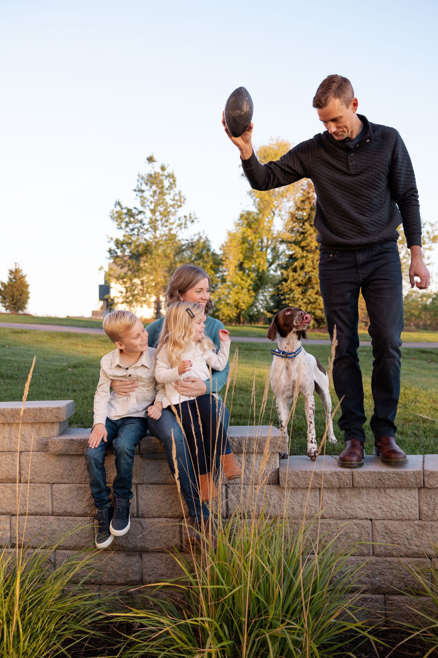 A playful family moment on a wall at sunset with their dog while holding a football.