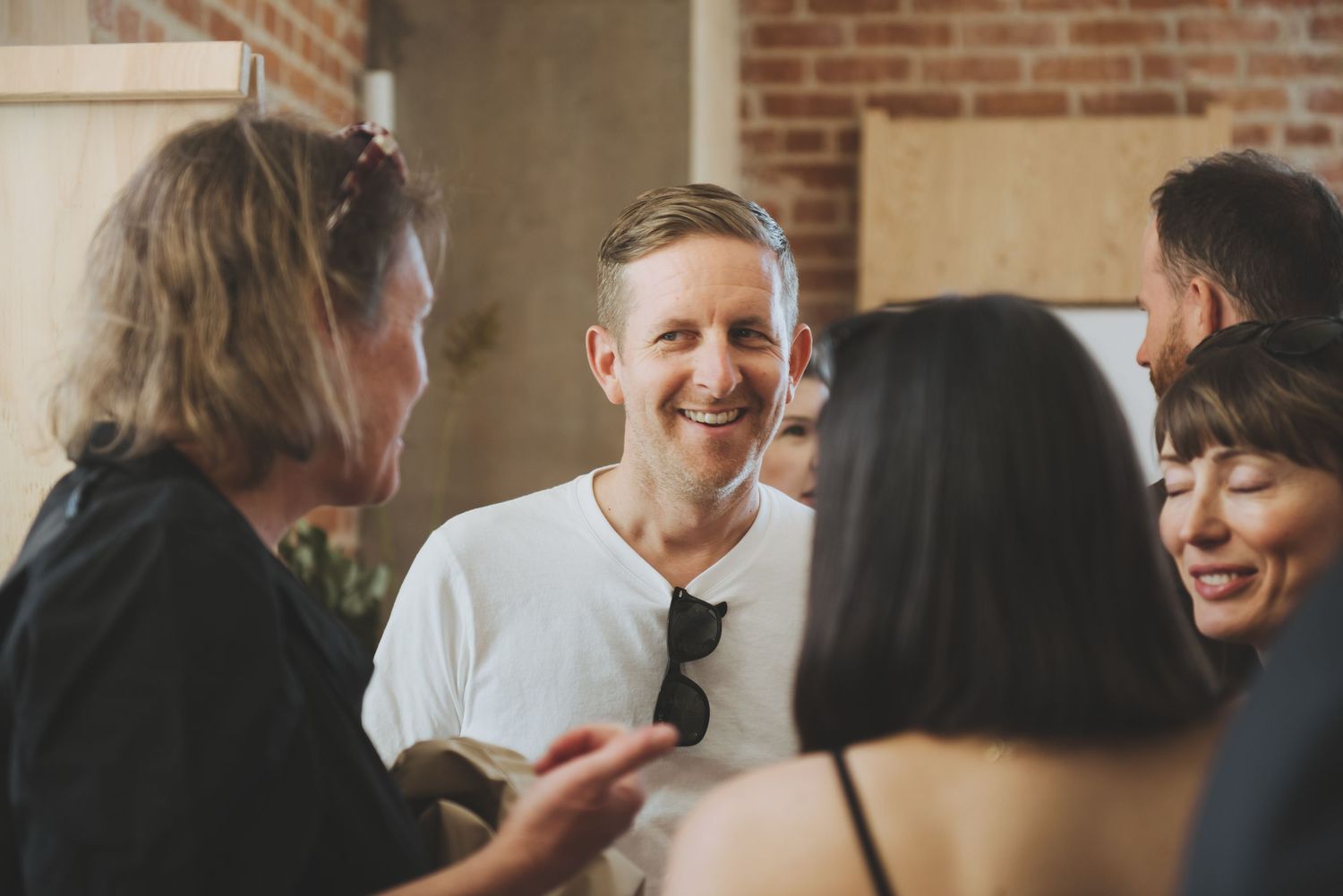 A group of people engaging in lively conversation at an indoor gathering with exposed brick walls in the background.