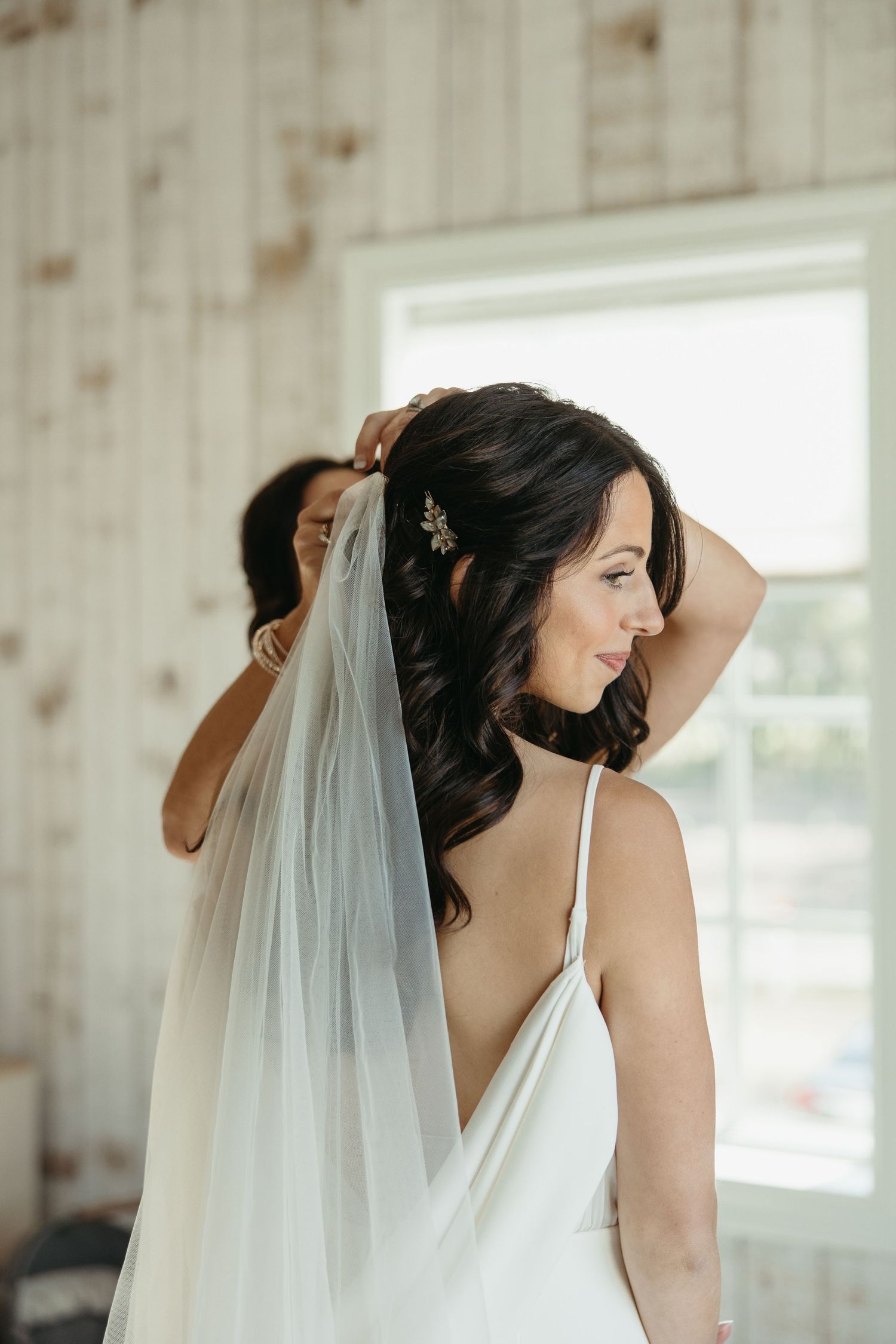 Back view of wedding dress and veil being styled in a light-filled room.