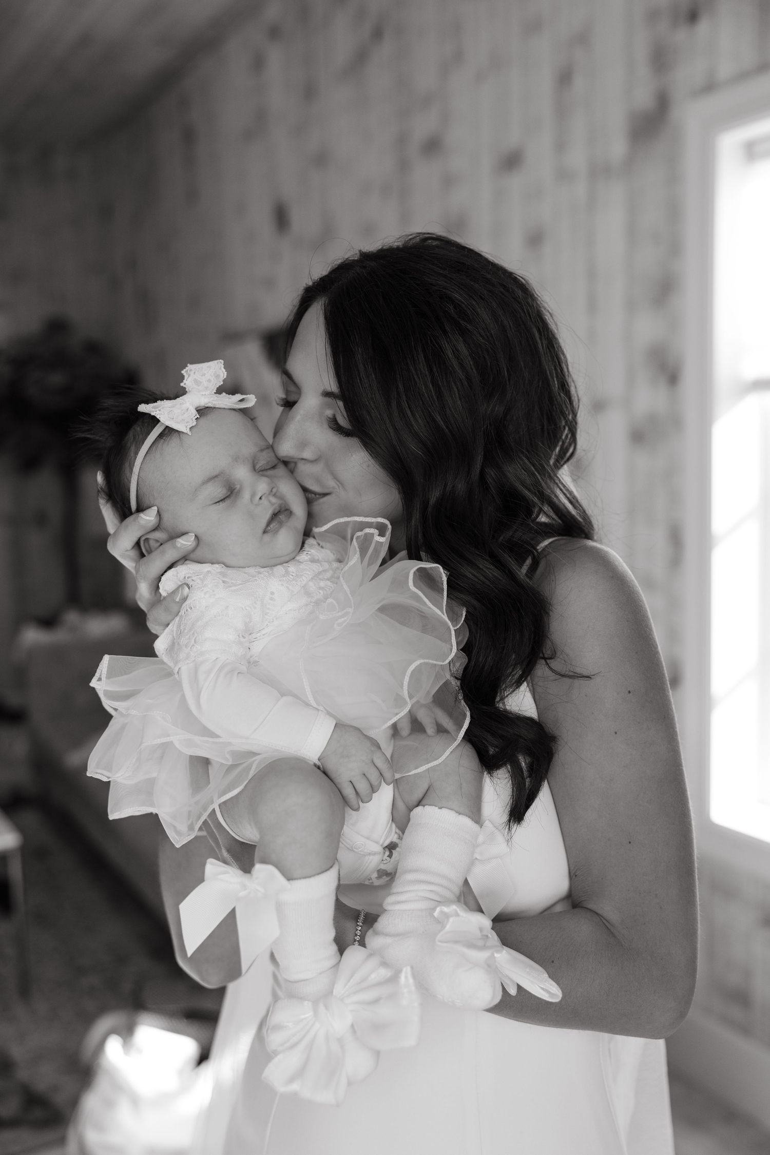 A tender black and white portrait of a mother and baby in white formal dress with ruffles.