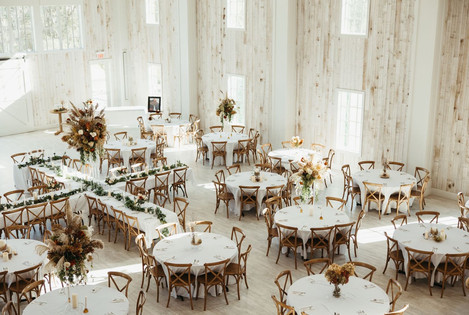 A bright wedding reception venue with rustic tables, chairs and floral centerpieces.