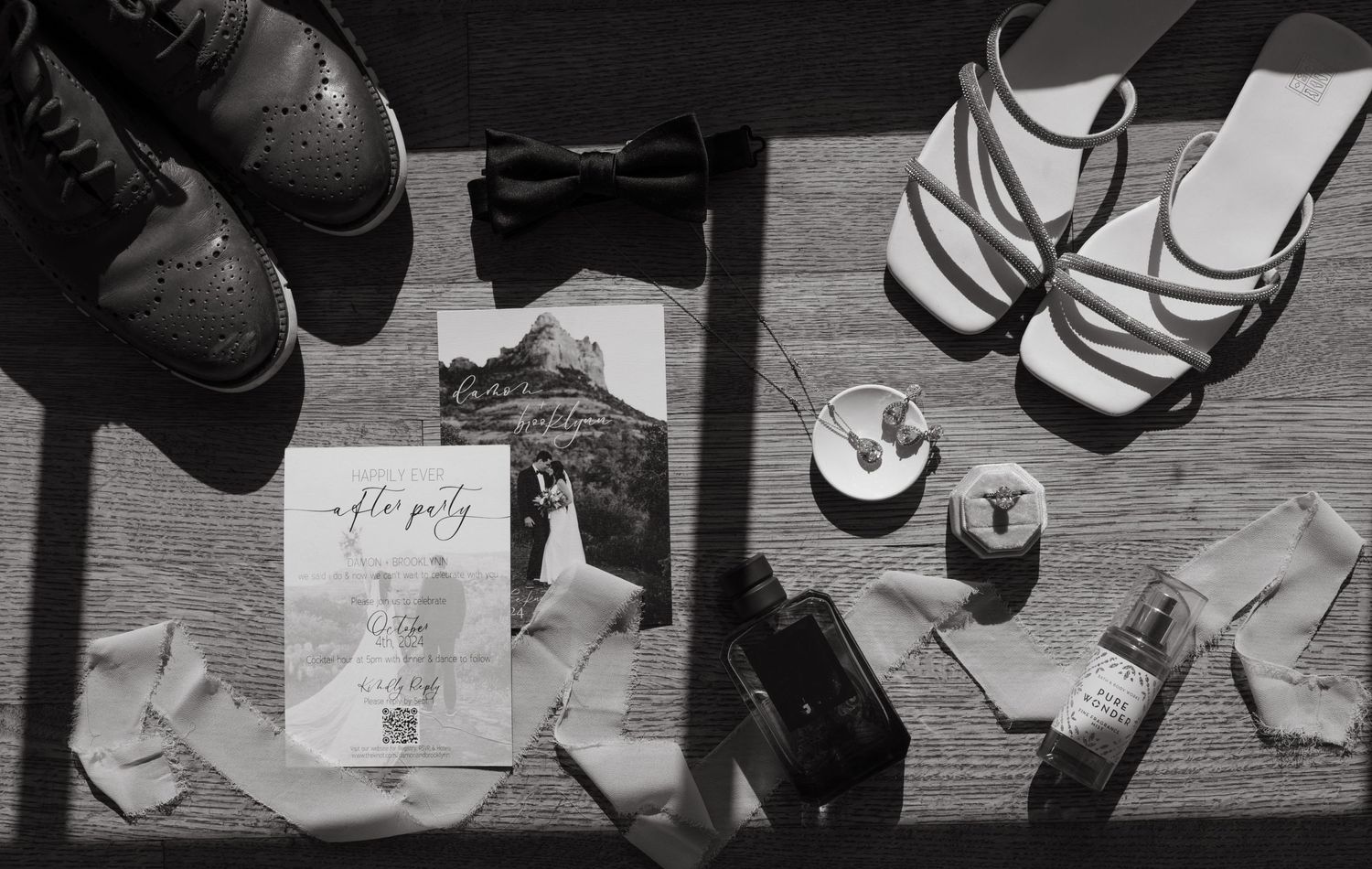 Black and white photo of wedding shoes and details arranged on a light surface.