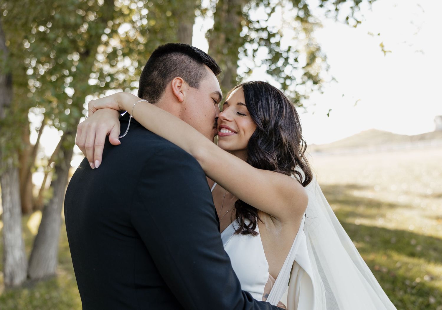 Newlywed couple sharing an intimate moment outdoors in sunlit natural setting.