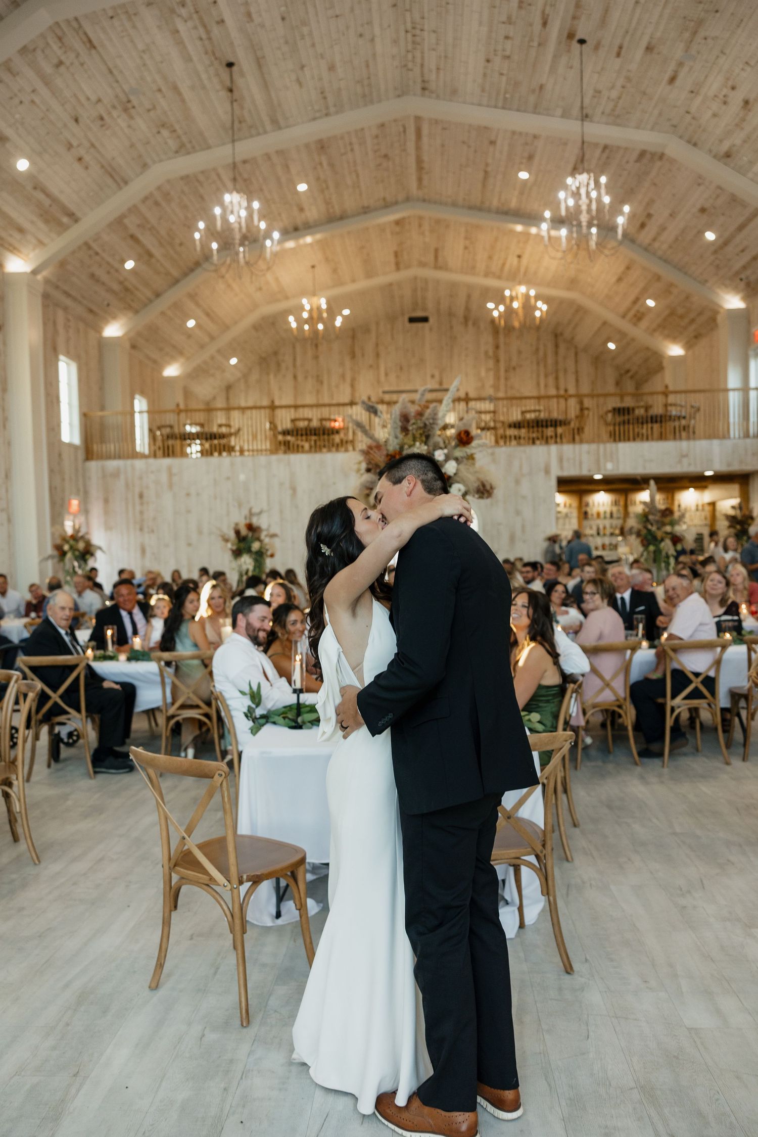 First dance in an elegant barn venue with wooden beams and crystal chandeliers.