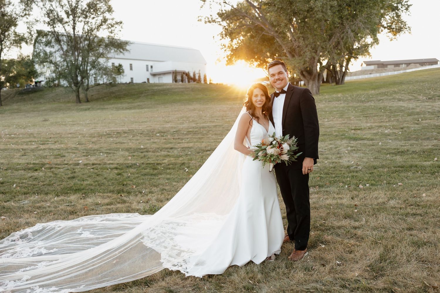 Sunset wedding portrait of couple with long flowing veil in golden light.