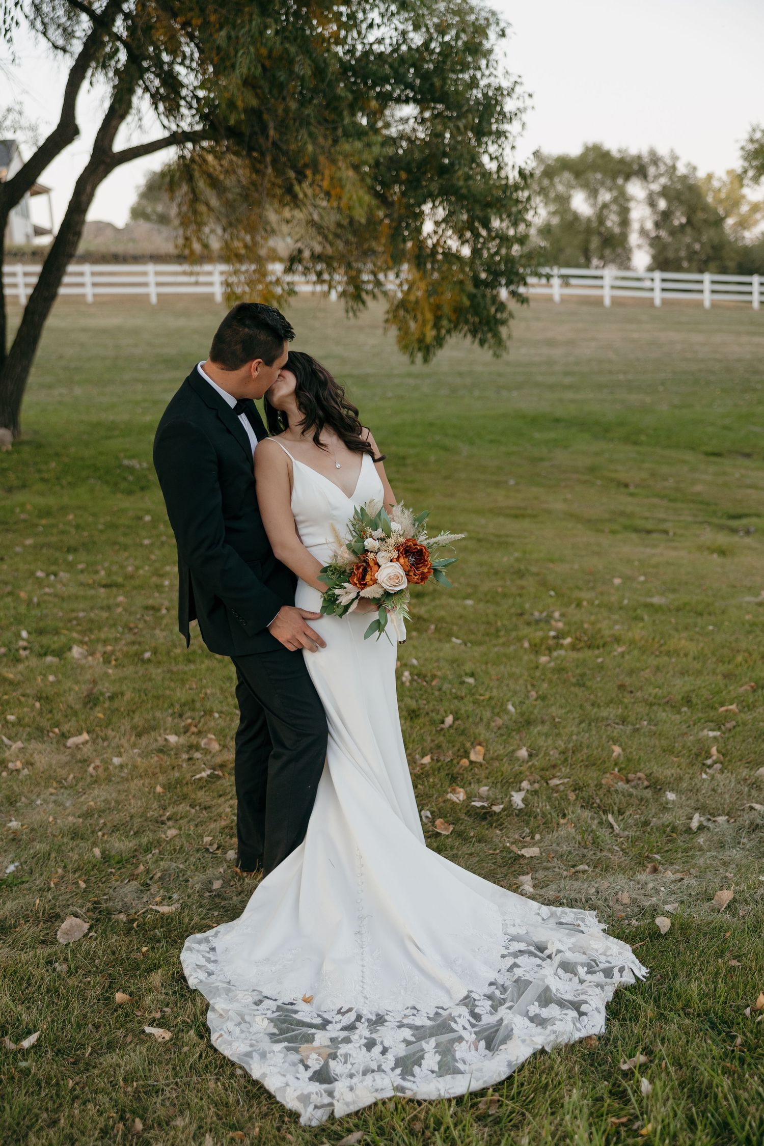 An elegant wedding photo featuring a lace-trained white dress against a rustic outdoor backdrop.