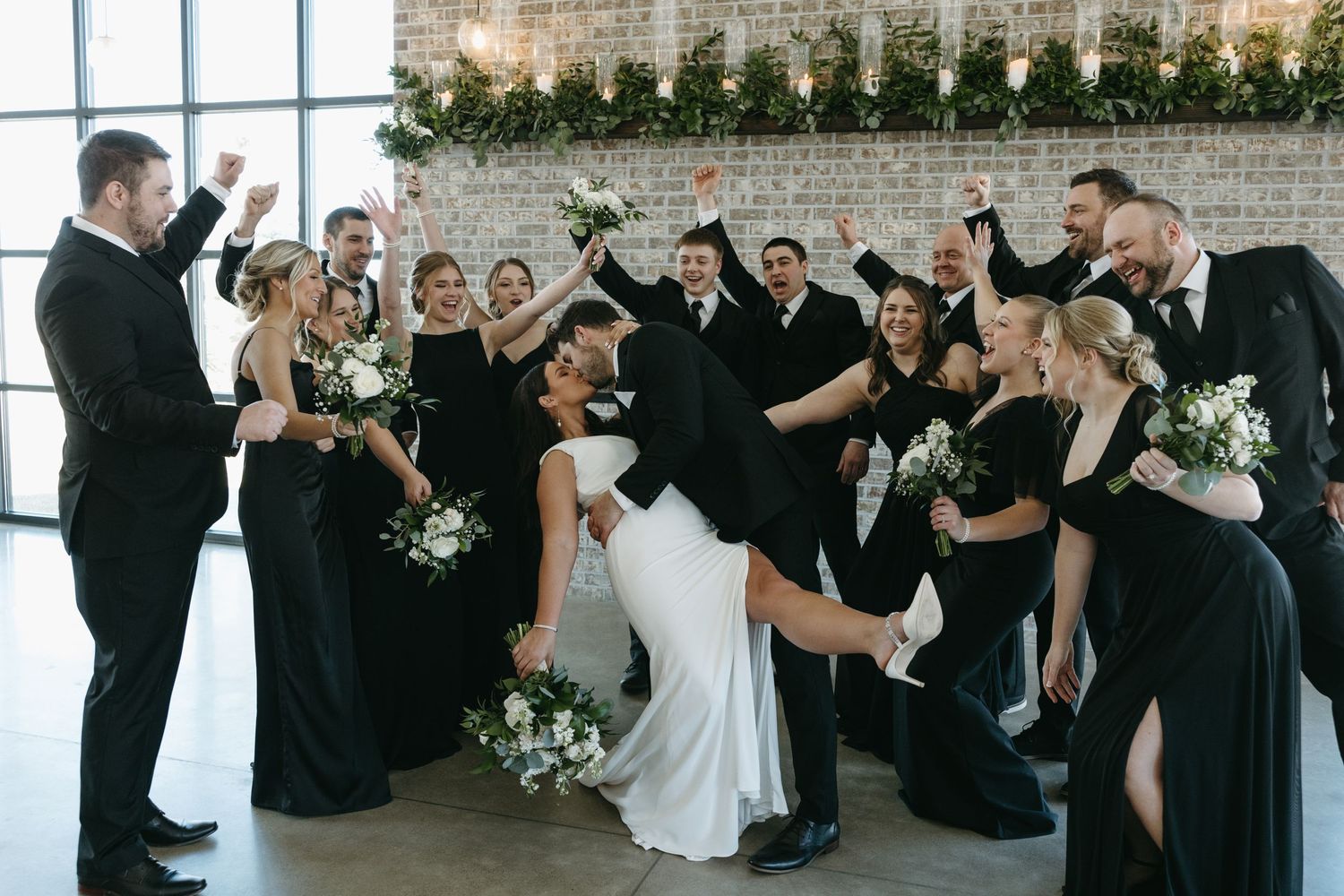 Wedding party celebrates with enthusiastic group pose in black formal attire.