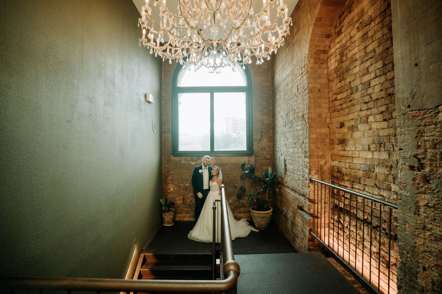 Wedding scene under crystal chandelier in industrial-style venue with brick walls.