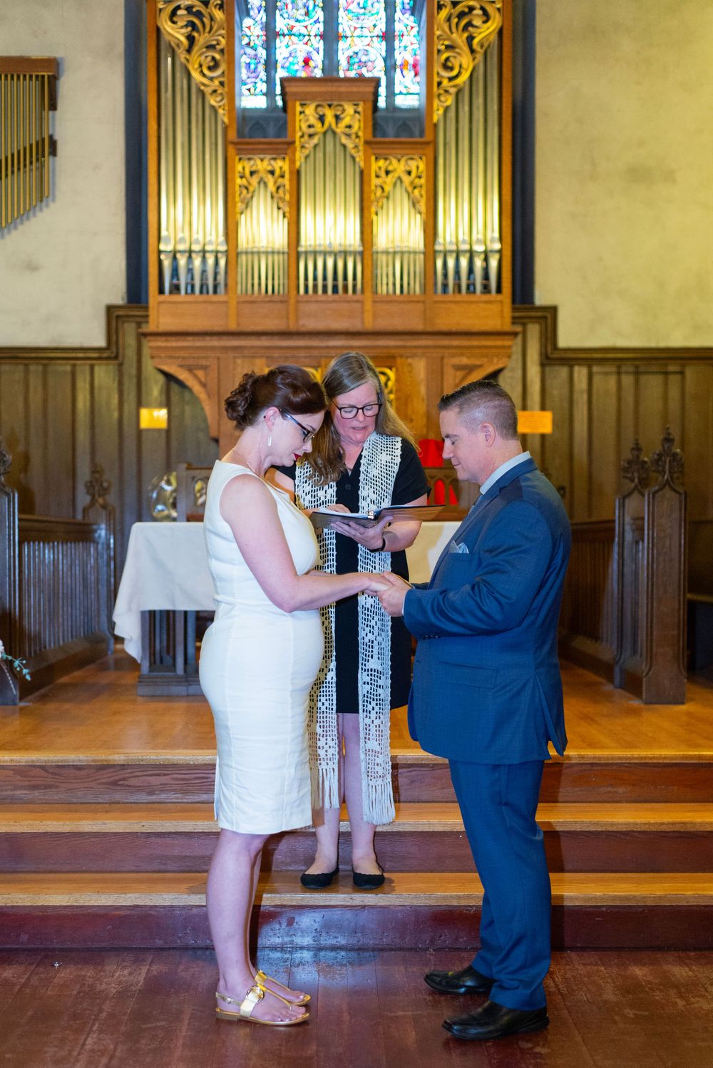 Wedding ceremony taking place in a chapel with ornate pipe organ and wooden interior details.