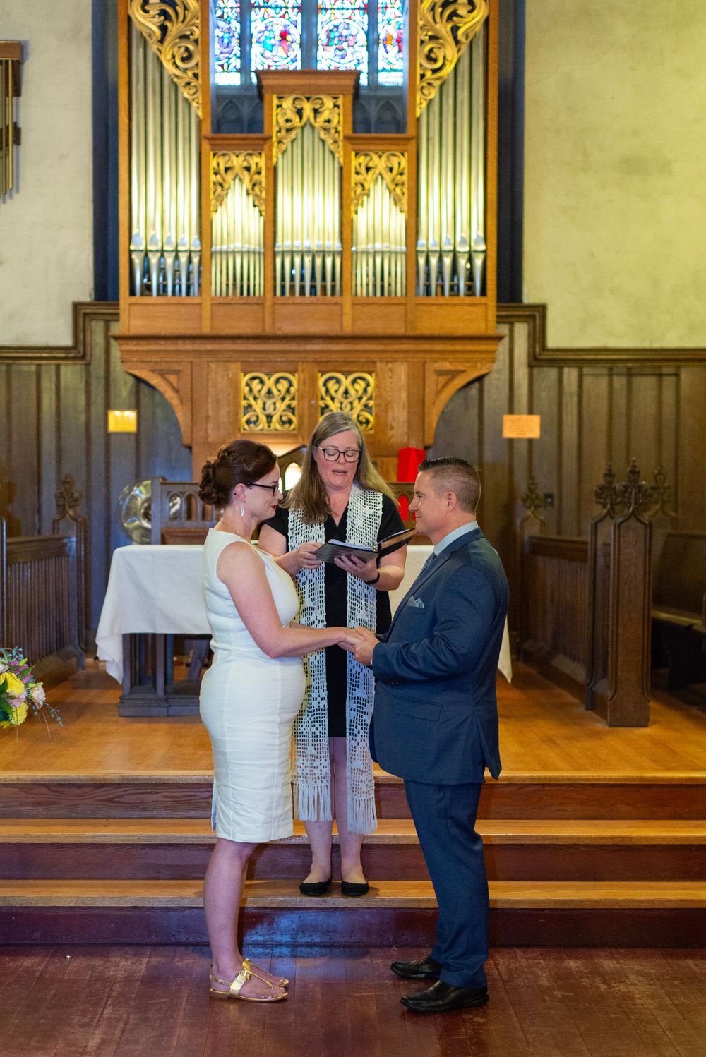 A wedding ceremony taking place in front of an ornate wooden church organ.