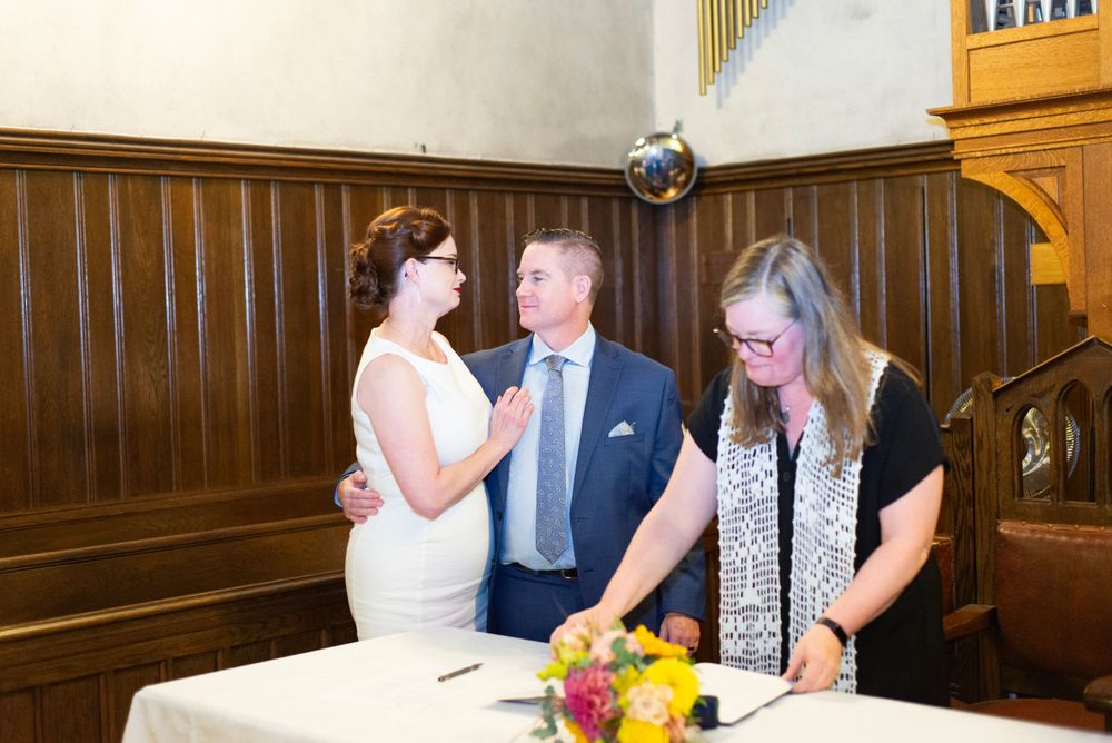 A couple signs their marriage certificate with an officiant during a wedding ceremony in a church hall.