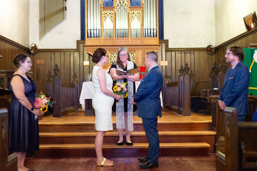 A wedding ceremony taking place in a church sanctuary with wooden paneling and an organ pipe backdrop.