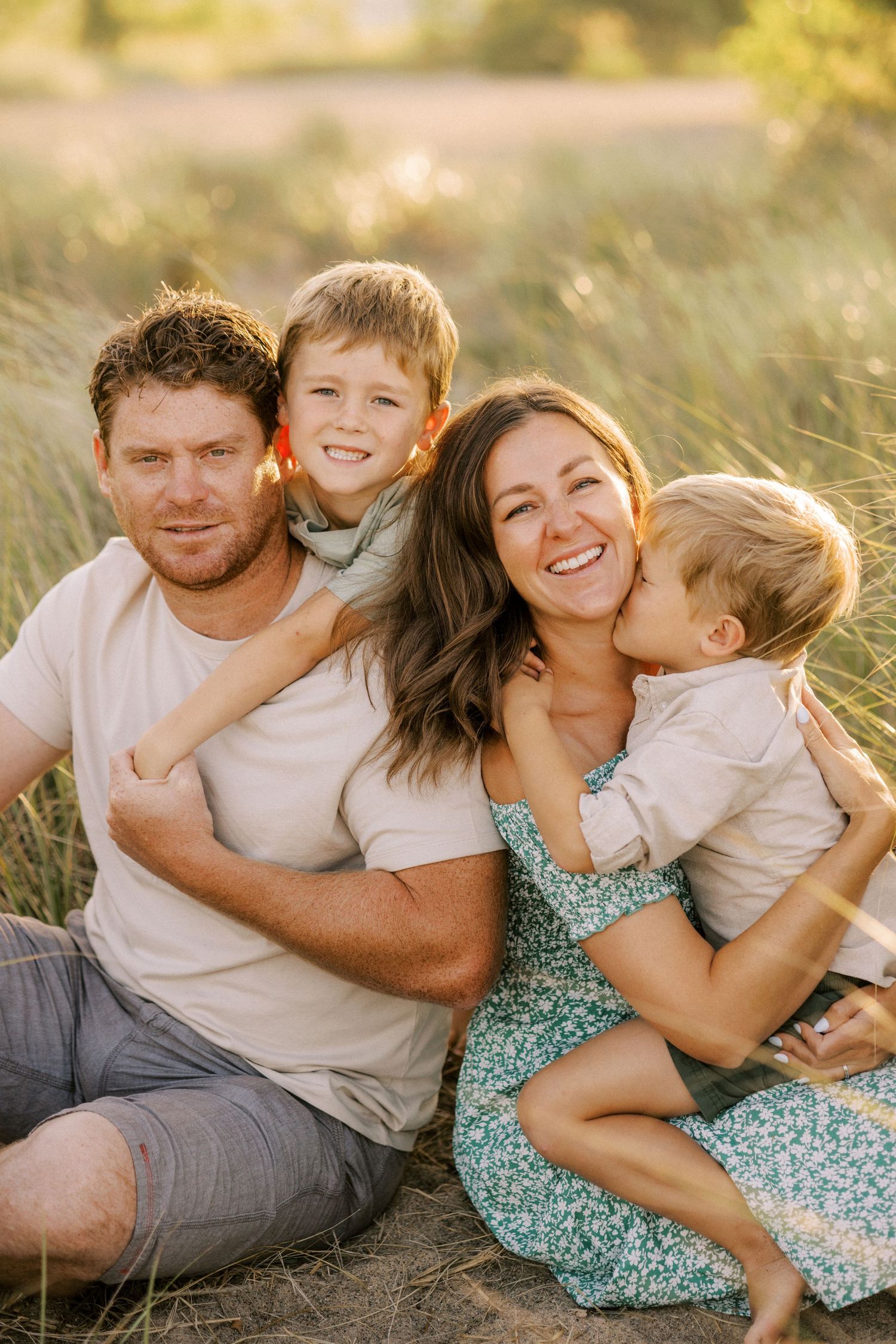 Happy family of four sitting close together in field during golden hour.