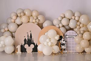 Neutral-toned balloon arch with Disney castle silhouette and Mickey Mouse decorations against white wall.