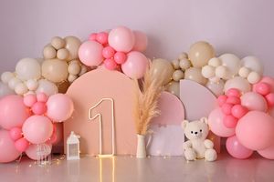 Pink and beige balloon arch with number 1 gold sign, teddy bear, and lanterns for first birthday party decoration.