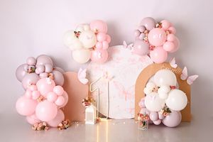 Pink and white balloon garland decorating a cake smash setup with butterfly accents and soft pastel tones.