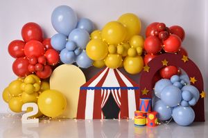 Circus-themed party backdrop with red, yellow, and blue balloon arch surrounding a miniature carnival tent decoration.