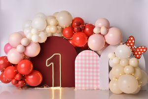 A festive balloon arch with pink, red, and white balloons decorated with gingham hearts against a burgundy wall.