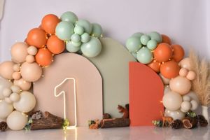 Orange and mint green balloon garland with wooden accents and number one decoration.