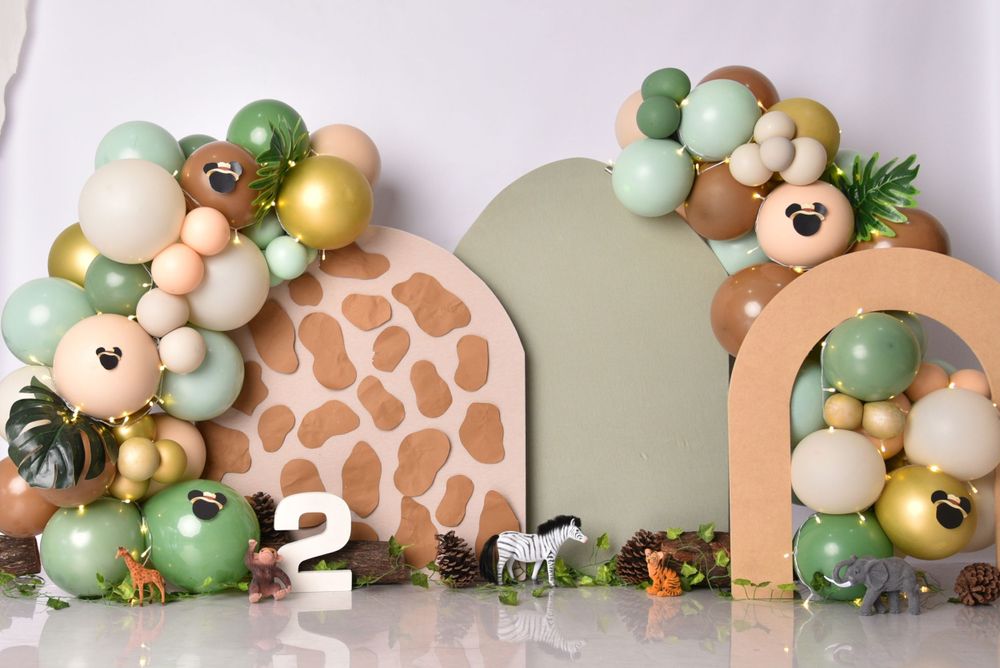 Safari-themed balloon arch with green and neutral tones featuring giraffe print panels and jungle decorations.