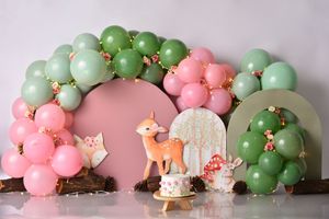 Pink and green balloon arches with woodland animal decorations create a whimsical baby shower backdrop against a blush wall.