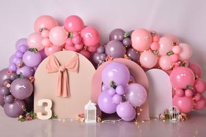 Pink and purple balloon garland decorates a wall with white letter decorations and soft lighting for a party setup.