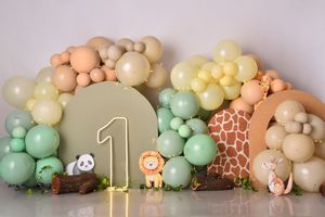 A pastel balloon garland arch with safari animal decorations and greenery creates a whimsical party backdrop.